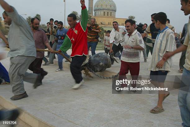 Iraqi civilians celebrate and drag the head of a Saddam Hussein statue through the streets after US Marines helped them take it down April 9, 2003 in...