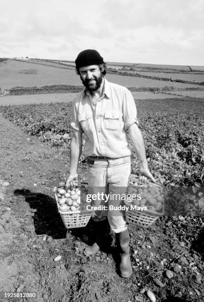 Portrait of an English potato farmer carrying baskets of potatoes to sell in a local market, in Devon, England, 1980. .