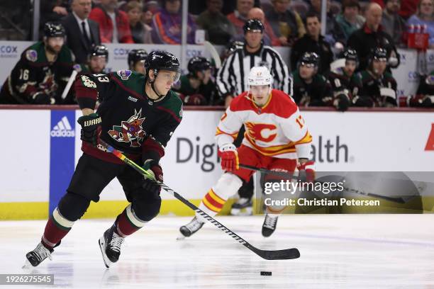 Travis Dermott of the Arizona Coyotes skates with the puck ahead of Yegor Sharangovich of the Calgary Flames during the first period of the NHL game...