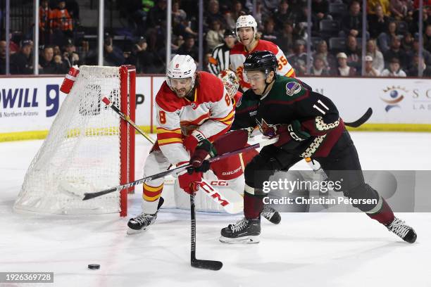 Dylan Guenther of the Arizona Coyotes and Chris Tanev of the Calgary Flames battle for a loose puck during the second period of the NHL game at...