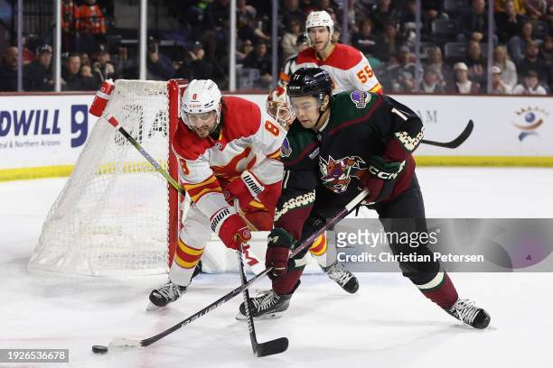 Chris Tanev of the Calgary Flames and Dylan Guenther of the Arizona Coyotes battle for a loose puck during the second period of the NHL game at...