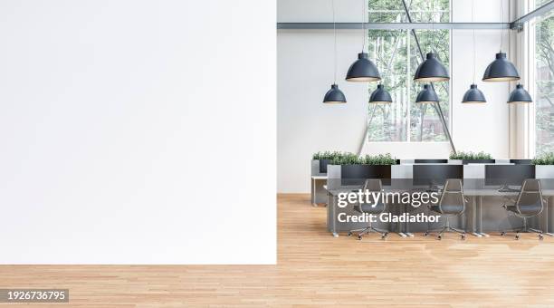 semi-empty office interior with white wall and copy space, work desks and large windows on hardwood floor - empty office wall stock pictures, royalty-free photos & images
