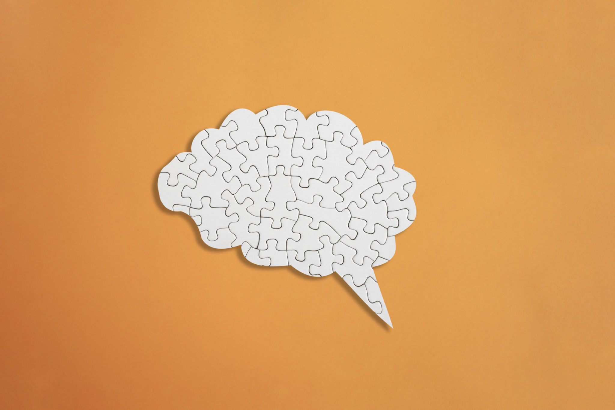 Brain shaped white jigsaw puzzle on orange background, mental health and problems with memory concept Brain shaped white jigsaw puzzle on orange background, mental health and problems with memory concept