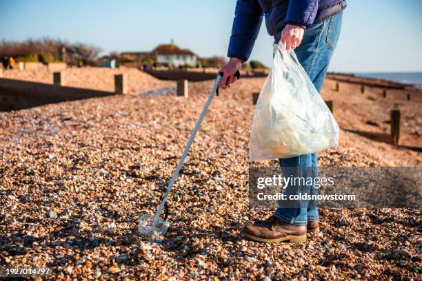 senior man cleaning plastic pollution from the beach - coastal feature stock pictures, royalty-free photos & images
