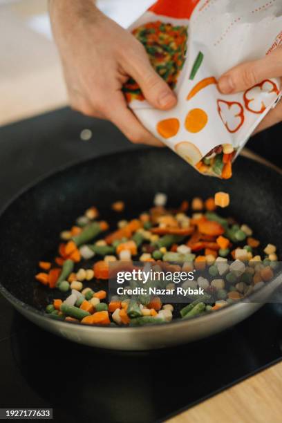 ein unbekannter mann gibt tiefkühlgemüse zum kochen in eine pfanne - gefrierkost stock-fotos und bilder