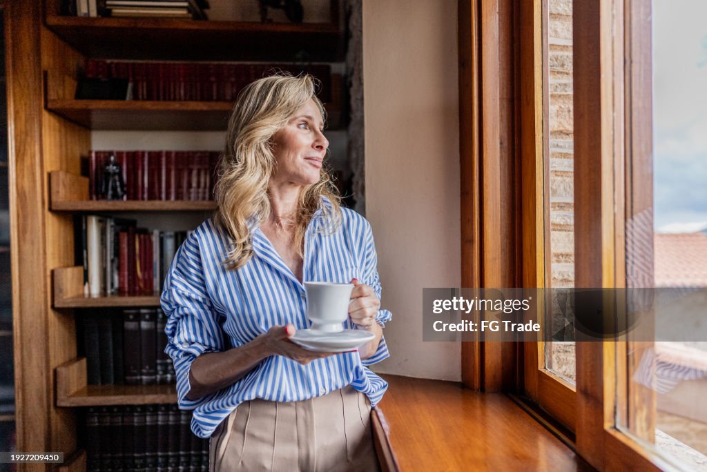 Mature woman contemplating while looking through the window at home