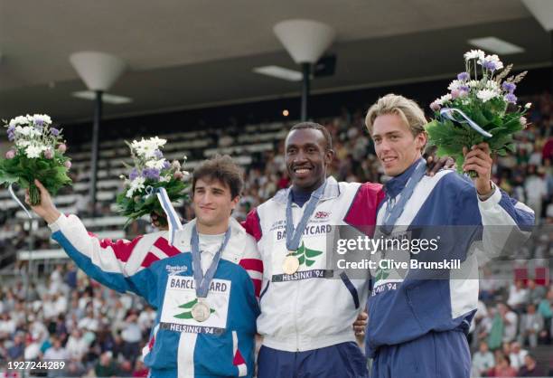 Linford Christie of Great Britain celebrates on the winners podium with gold medal alongside silver medalist Geir Moen from Norway and bronze...