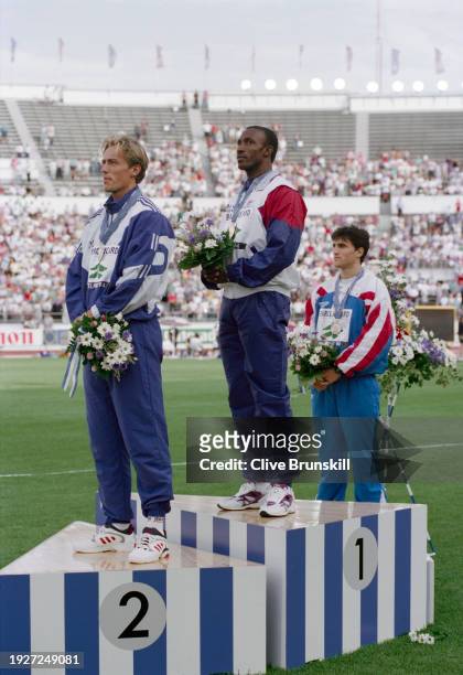 Linford Christie of Great Britain celebrates on the winners podium with gold medal alongside silver medalist Geir Moen from Norway and bronze...
