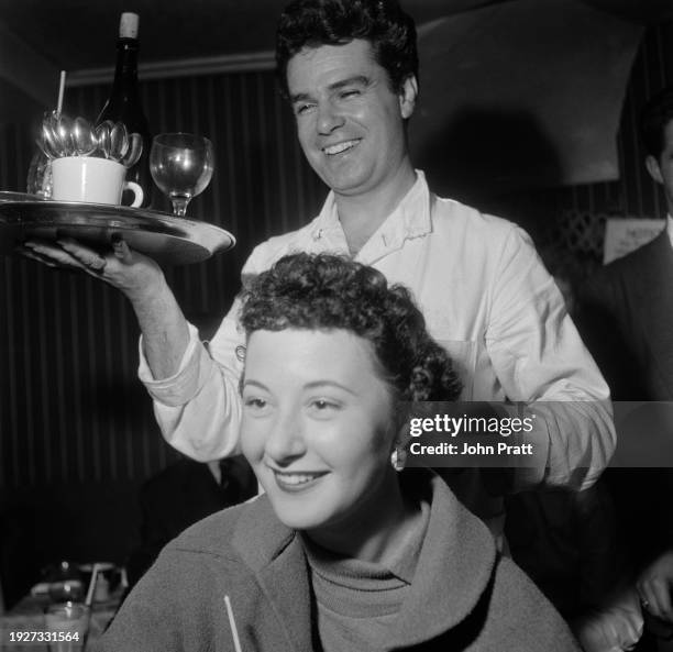 Waiter holding a tray stands behind a woman at the Moulin Rouge, a nightclub in a Soho basement, London, August 1954. The woman is named as Sandra...