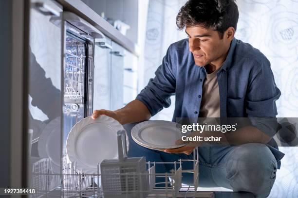 young man taking washed plates into the dishwasher - dishwasher stock pictures, royalty-free photos & images