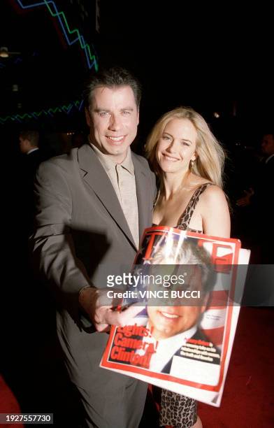 Actor John Travolta holds a Time Magazine with his picture on the cover as he arrives with his wife, actress Kelly Preston, at the world premiere of...