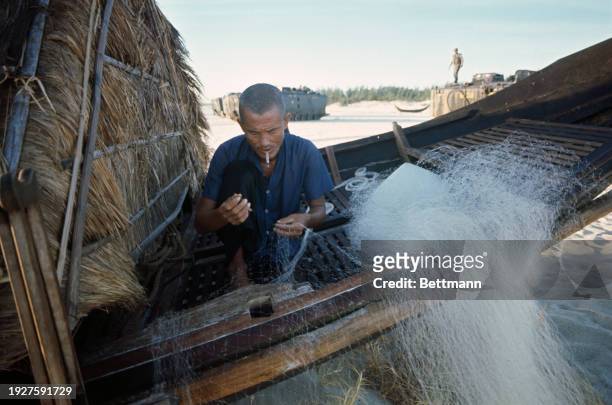 Vietnamese man mends his fishing nets as a US amphibious task group lands along the coast of South Vietnam, 15 miles north of Hue, July 20th 1967....