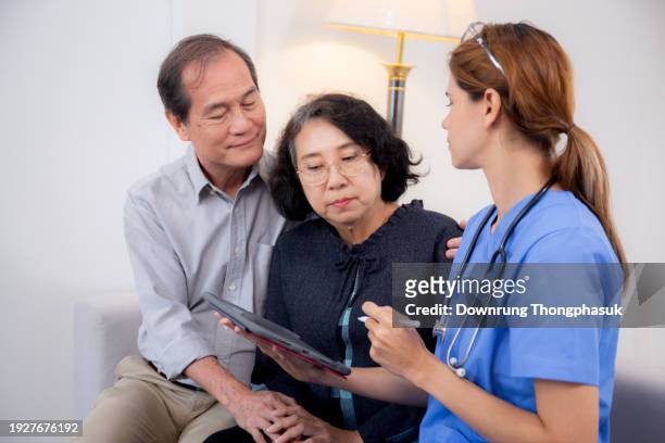 caregiver sitting on sofa checkup and diagnostic with elderly couple patient about health in living room at home, caretaker sitting on couch explaining and examining senior, insurance and medical. - gerontology stock-fotos und bilder