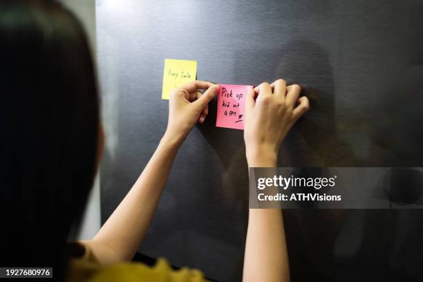 mujer que pone en blanco la lista de tareas en la puerta del refrigerador en la cocina - imán fotografías e imágenes de stock