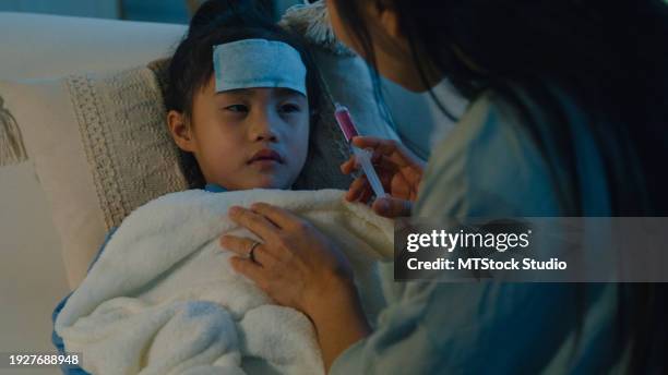 mom takes care of her daughter who gets sick and has a high fever and feeds liquid medicine via syringe in the nighttime at home. illness girl with a medical condition and family wellness. - medicina para los resfriados fotografías e imágenes de stock