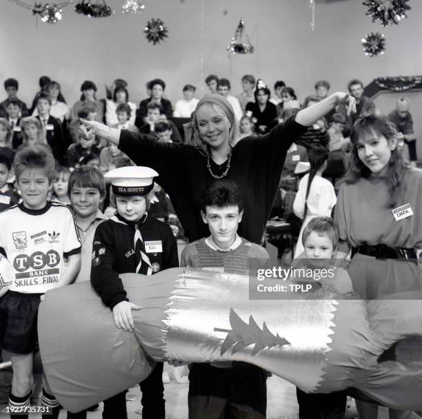 Portrait of British radio television personality Sarah Kennedy poses with child guests on set of the Thames Television show, 'Daytime' , London,...