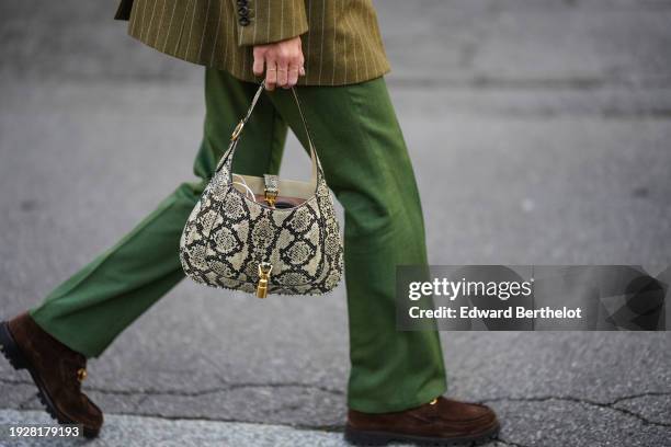 Guest wears green flared pants, brown shoes, a beige and black snake print Gucci bag, outside Gucci, during the Milan Fashion Week - Menswear...