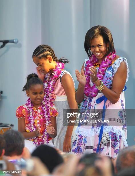 First Lady Michelle Obama applauds while standing on stage with daughters Sasha and Malia while US President Barack Obama speaks during the luau for...