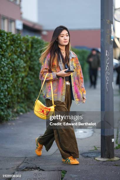 Guest wears a tie and dye colored denim jacket, a yellow bag, khaki flared wide-leg pants, Asicas sneakers shoes, outside Gucci, during the Milan...