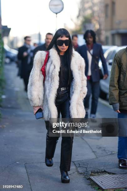 Guest wears sunglasses, a white fluffy winter coat, studded belt, black leather pants, leather shoes, outside Gucci, during the Milan Fashion Week -...