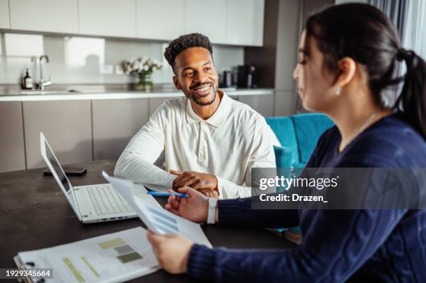 smiling african american and middle eastern mid adult couple discussing long term investing. married couple sorting finances and bills together - long term investment stockfoto's en -beelden