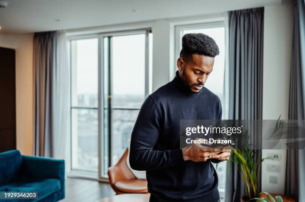 serious afro-caribbean or african mid adult man using smart phone in modern office or apartment - afro caribbean people stock pictures, royalty-free photos & images