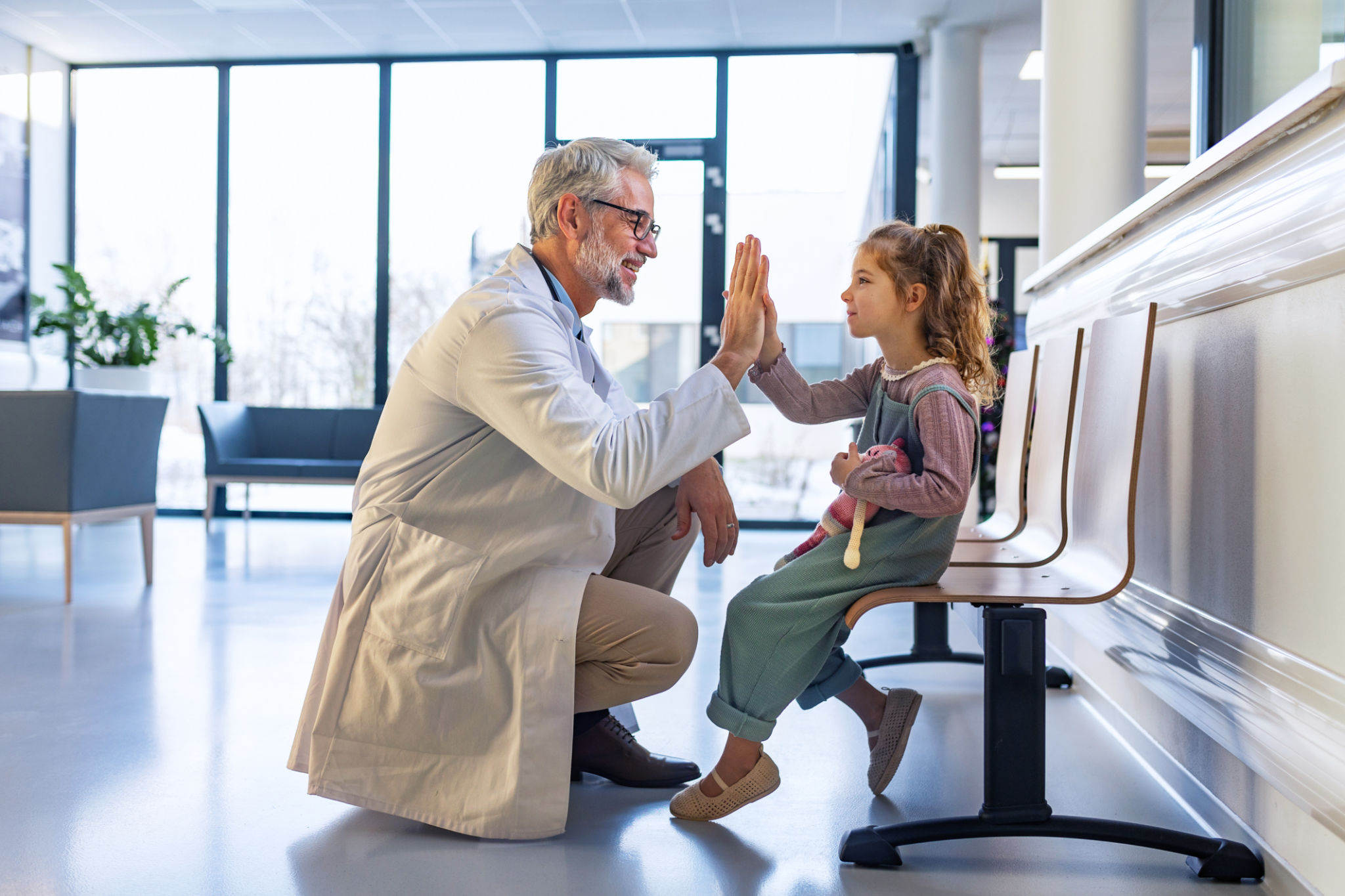Friendly pediatrician giving high five to little patient. Cute preschool girl in greeting doctor in hospital corridor. Friendly pediatrician giving high five to little patient. Cute preschool girl in greeting doctor in hospital corridor.