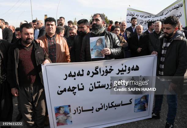 Protesters hold pictures of children bodies and a banner reading "Arbil remains resilient and it does not kneel down to terrorist attacks" during a...