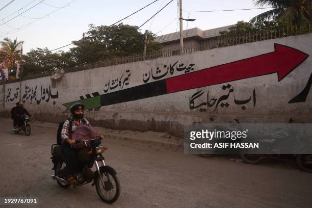 Motorcyclists ride past the Pakistan People's Party symbol painted on a wall along a street in Karachi on January 16 ahead of the country's upcoming...