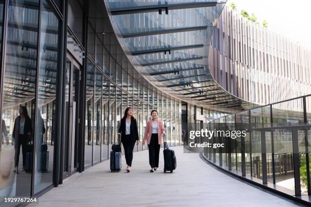 two young asian female travelers walking with wheeled luggage at airport terminal - kuala lumpur airport stock pictures, royalty-free photos & images