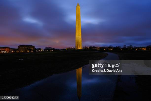 The Washington Monument is reflected in a rain puddle as the city lights cast a glow on the low-lying clouds before daybreak and after an overnight...