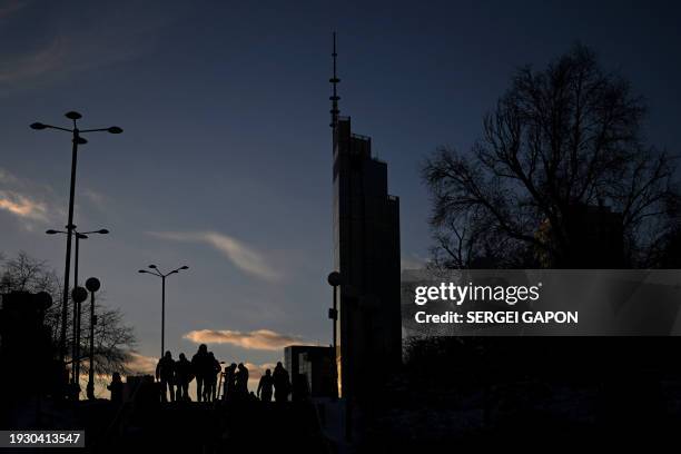 Pedestrians walk down a street in front of a skyscraper as the sun sets in Warsaw, Poland on January 16, 2024.