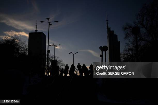 Pedestrians walk down a street in front of a skyscraper as the sun sets in Warsaw, Poland on January 16, 2024.