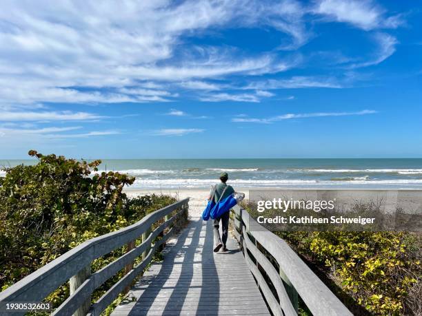 hombre mayor que lleva sillas de playa sobre el sendero contra la arena, el agua y los cielos azules - tampa fotografías e imágenes de stock