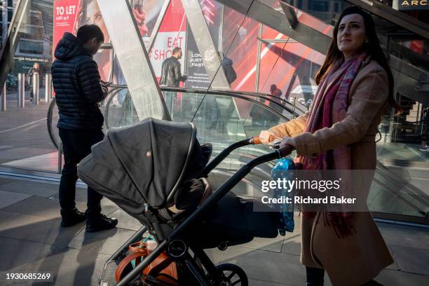 Mother with a child in an urban landscape of reflections and diagonals at the top of escalators in the City of London, the capital's financial...