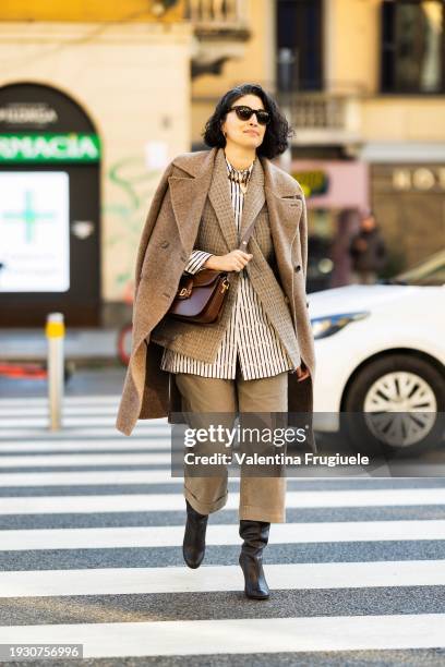 Caroline Issa is seen wearing brown leather boots, light beige straight trousers, black sunglasses, gold hoop earrings, a brown and white striped...
