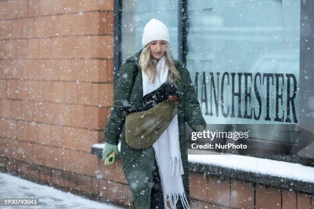 Woman is carrying her dog after heavy snowfall in Manchester City Centre, on January 16, 2024.