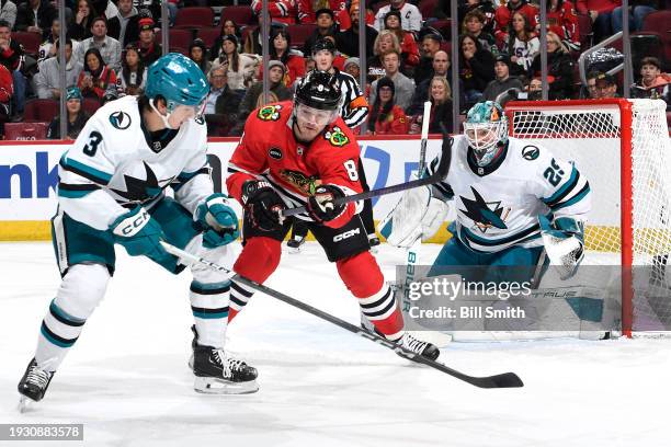 Henry Thrun of the San Jose Sharks and Ryan Donato of the Chicago Blackhawks eye the puck as Mackenzie Blackwood of the San Jose Sharks guards the...