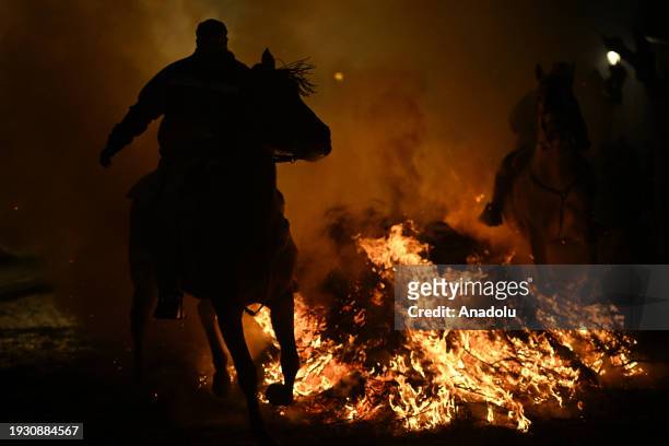 Men ride horses through a bonfire made of pine branches after the horses have been blessed by a priest to protect and purify them for the coming...