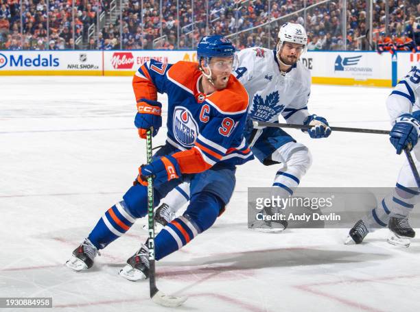 Connor McDavid of the Edmonton Oilers skates against Auston Matthews of the Toronto Maple Leafs with the puck during the game at Rogers Place on...