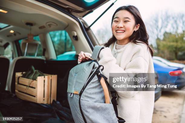 cheerful teenage girl putting her bag into the car trunk after checking out from the hotel - wonderlust stock-fotos und bilder