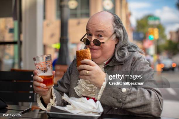 medium close up of benjamin franklin impersonator with philly cheesesteak and glass of beer - philadelphia stock pictures, royalty-free photos & images