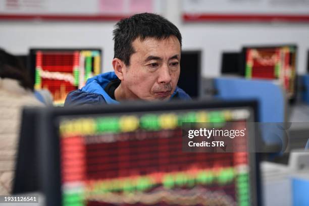 An investor looks at screens showing stock market movements at a securities company in Fuyang in China's eastern Anhui province on January 17, 2024....