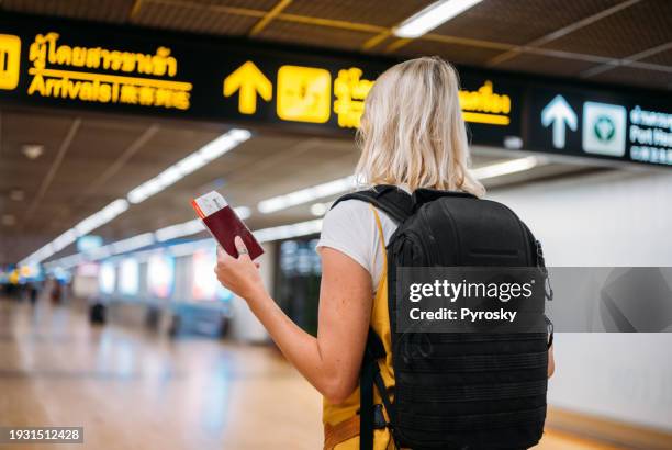 a woman at the airport holding a passport with a boarding pass - auswanderung und einwanderung stock-fotos und bilder