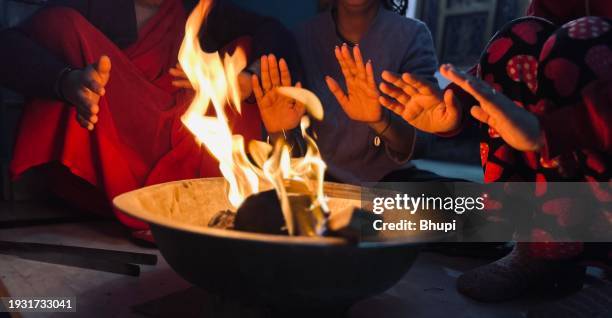 people warming hands while sitting around a bonfire in winter at home. - lohri festival imagens e fotografias de stock