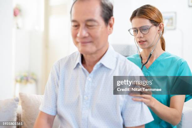 conducting a basis assessment to prevent geriatric diseases. a female home nurse examined a male patient's back with a stethoscope for general disease assessment in the living room during a home visit. - respiratory disease stock pictures, royalty-free photos & images