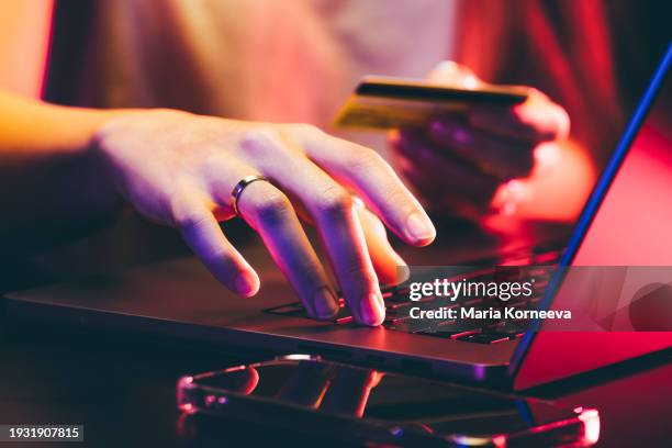 hands holding a credit card and using a laptop under neon light. online shopping. - ama-de-casa-comprando fotografías e imágenes de stock