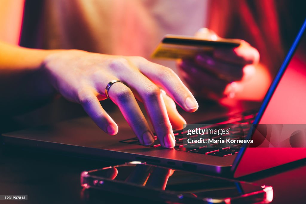 Hands holding a credit card and using a laptop under neon light. Online shopping.