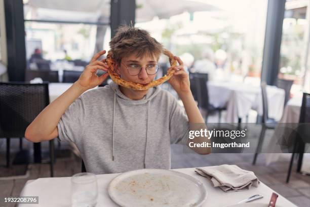ragazzo adolescente che mangia la pizza in un modo insolito e divertente - eccentrico foto e immagini stock
