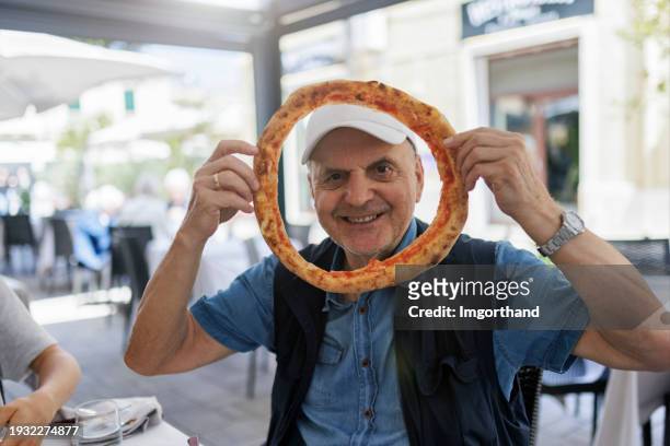 senior man have eaten a pizza and is smiling through the pizza edge  at the camera - pizza crust stock pictures, royalty-free photos & images